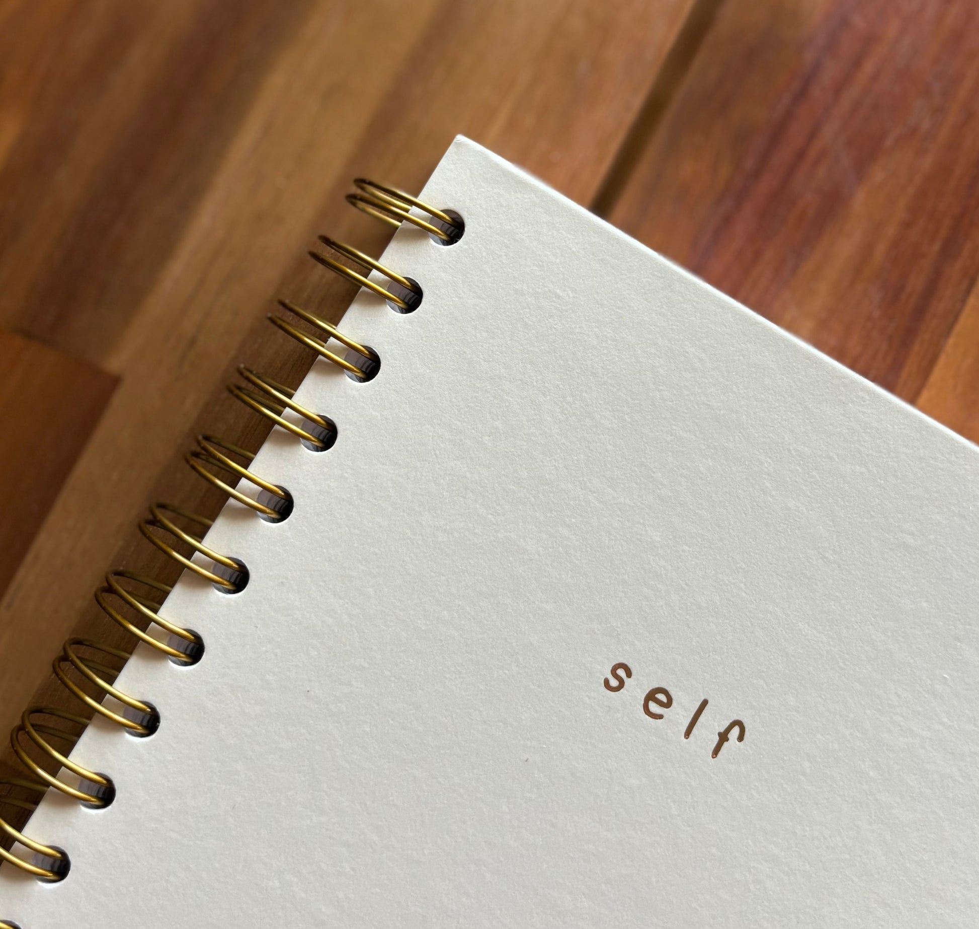 close-up view of details on cover of 'self' journal featuring a yellowish cream colored hardcover with gold lettering and gold spiral 